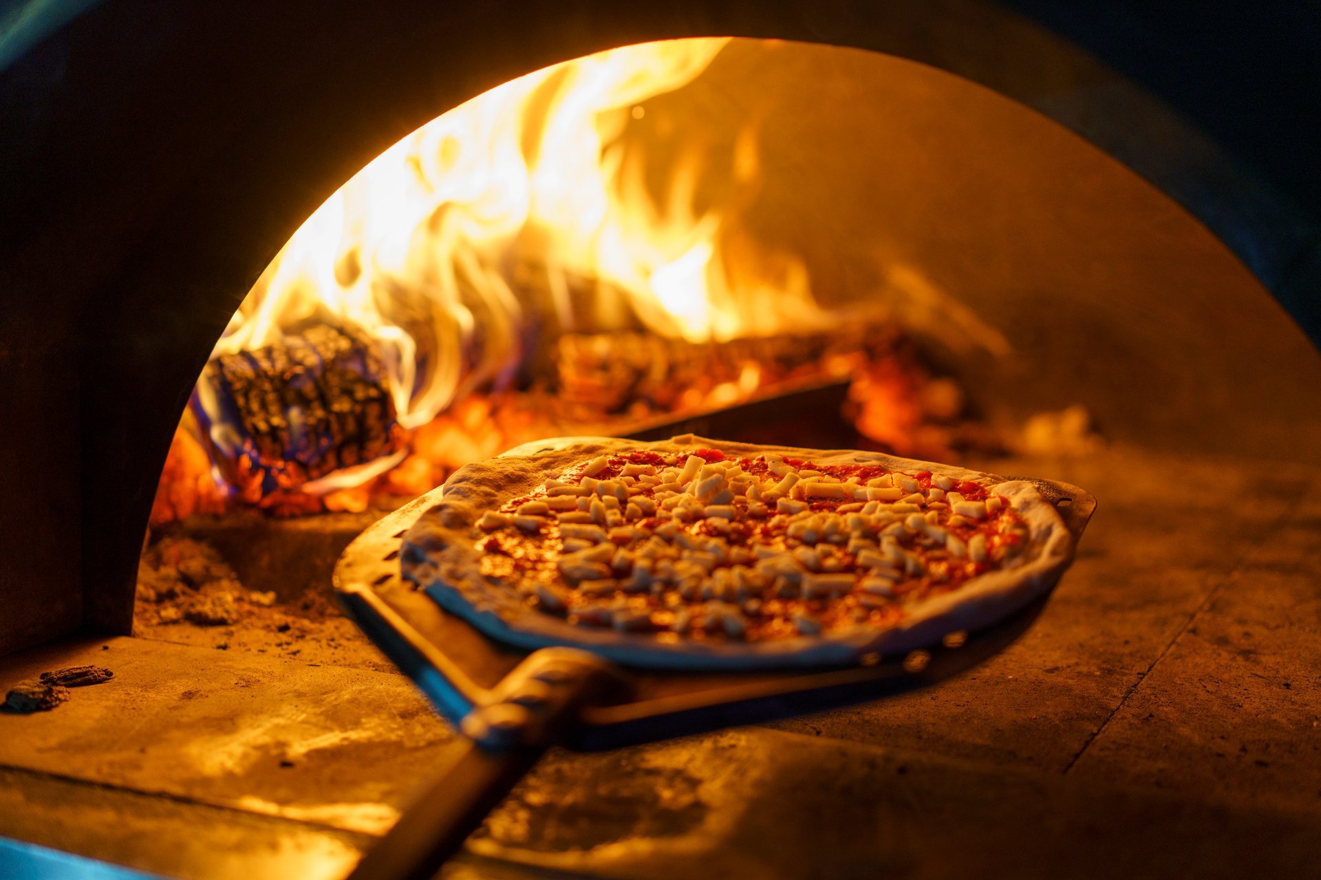 A chef places a freshly prepared pizza ready to be cooked in a wood fire pizza oven