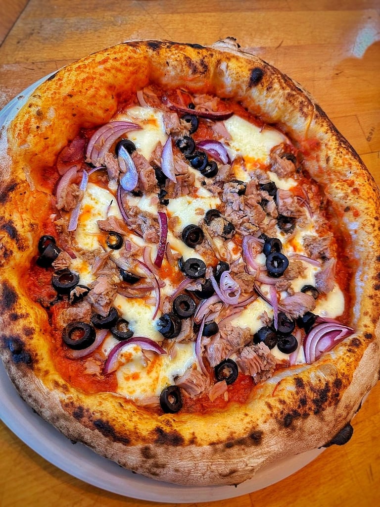 Freshly baked pizza with meat, black olives, red onions, and melted cheese on a charred crust, served on a white plate