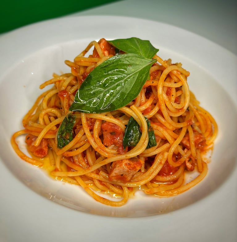 Spaghetti with tomato sauce, fresh basil leaves, and diced tomatoes on a white plate
