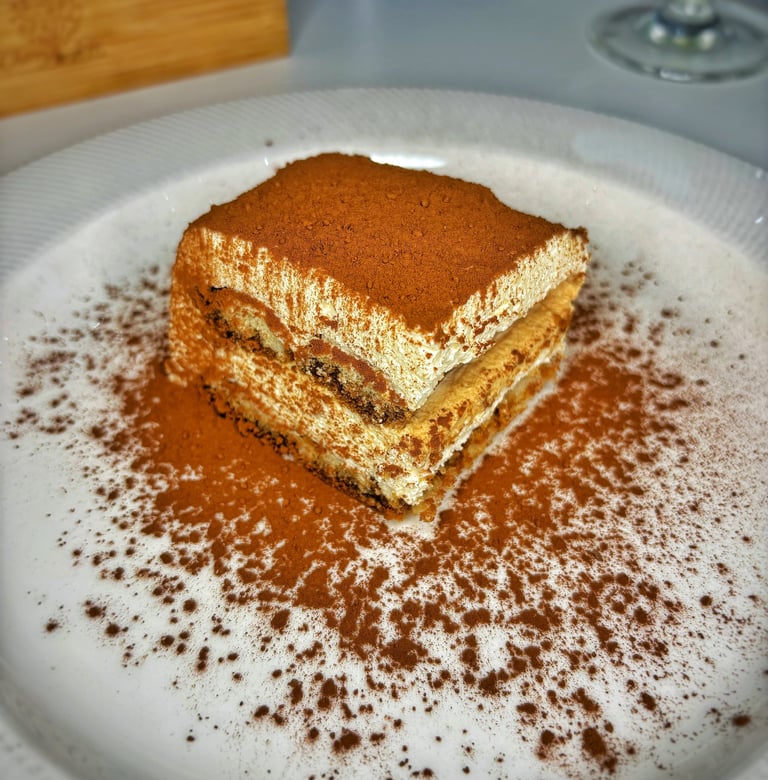 Square slice of tiramisu cake with cocoa powder dusting on a white plate