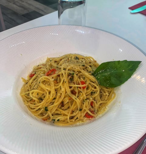 Plate of pesto spaghetti with red peppers and fresh basil leaf on white ribbed plate