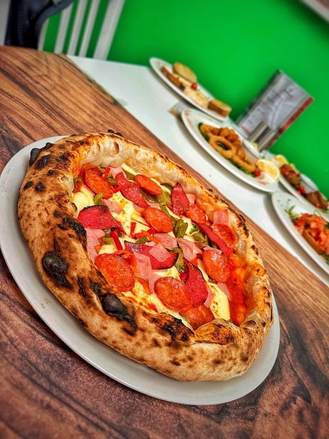 Freshly baked Neapolitan pizza with pepperoni, cheese, and herbs on white plate against green background