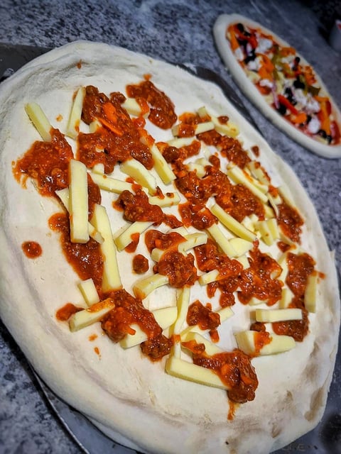 Unbaked pizza dough topped with red sauce, sliced potatoes, and pepperoni on a gray surface