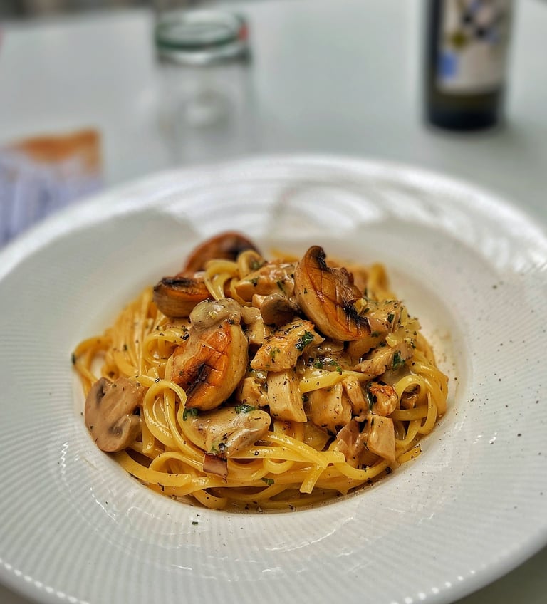 Plate of spaghetti with sautéed mushrooms and herbs in a white bowl with glasses and bottle in background