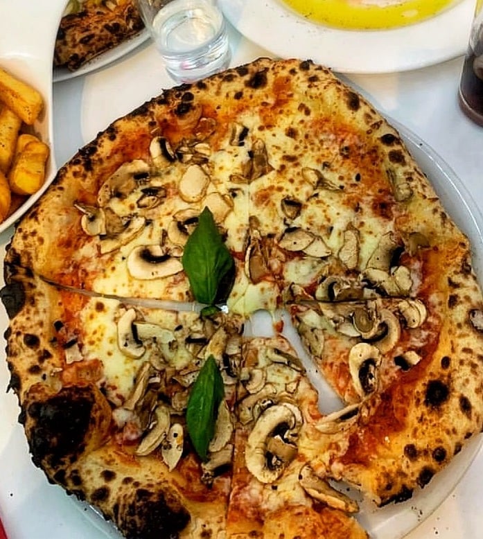 Wood-fired pizza with sliced mushrooms, melted cheese, fresh basil, and charred crust on a white plate