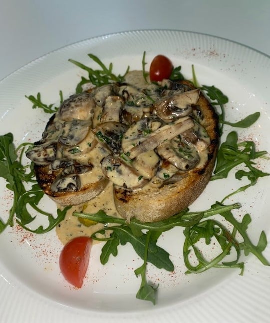 Gourmet open-faced sandwich with sautéed mushrooms on toasted bread, garnished with arugula and tomato slices on white plate