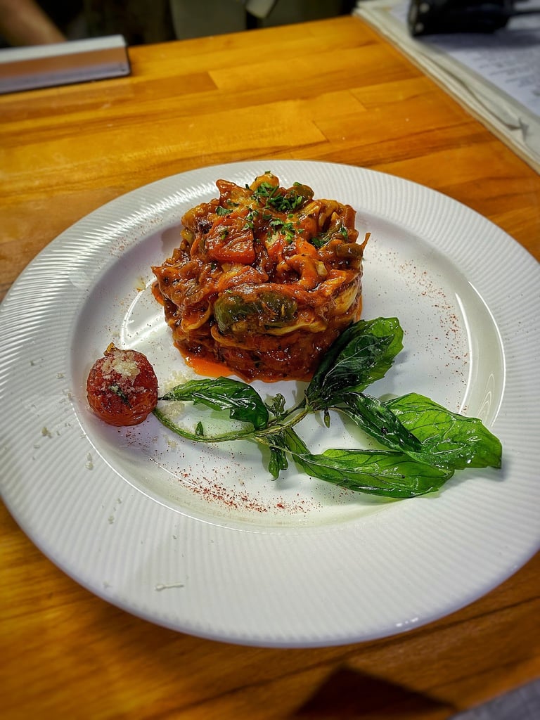 Plated fine dining dish with crispy fried pasta tower, fresh basil leaves, and red sauce on wooden table