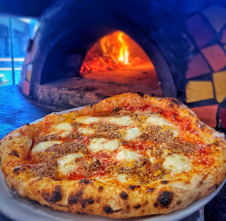 Traditional Neapolitan pizza with cheese and herbs in front of a wood-fired oven with glowing flames
