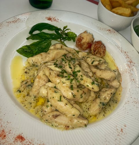 Sliced chicken breast in olive oil and herb sauce, garnished with fresh basil and paprika on a white plate